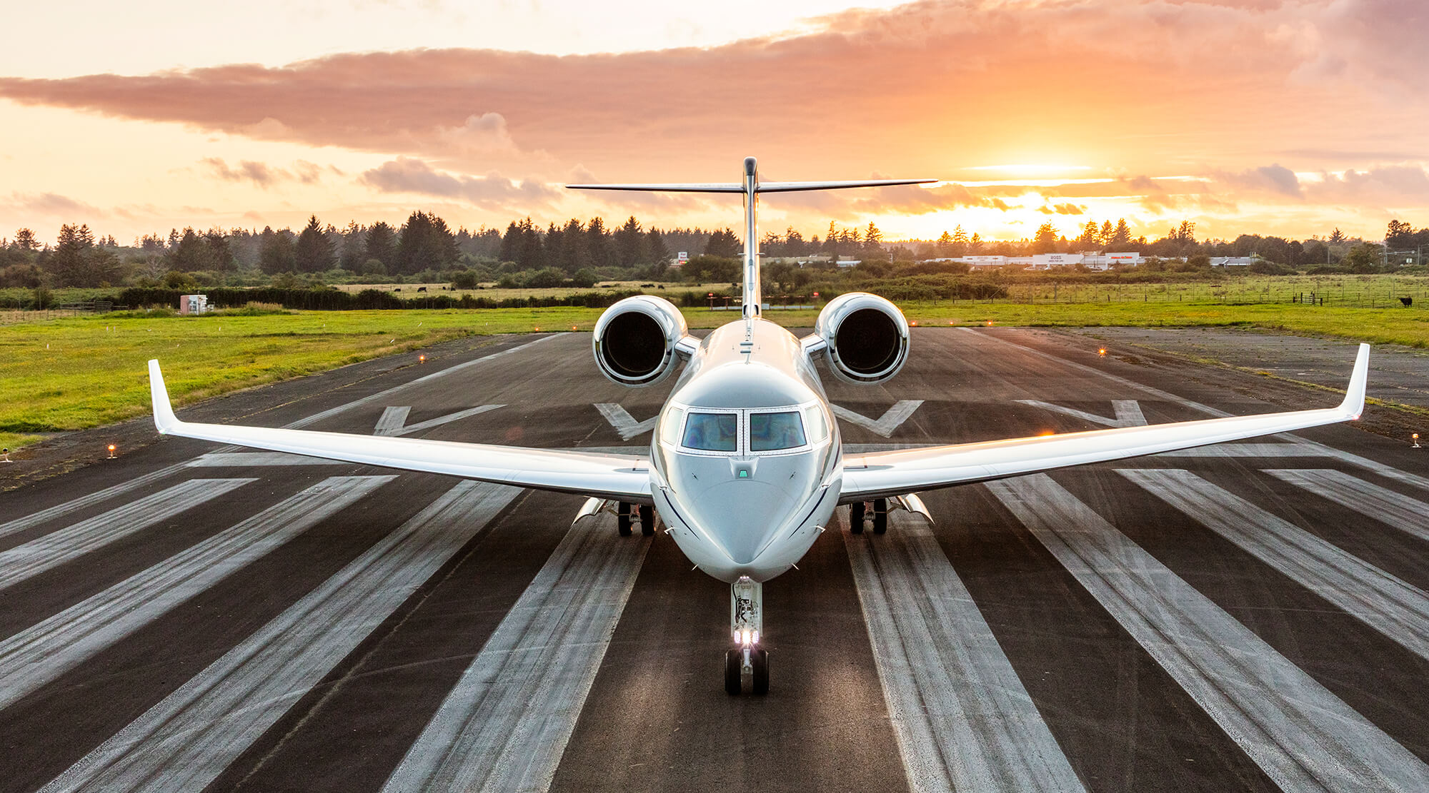 G500 aircraft parked on taxiway at sunrise with green fields and trees in the distance