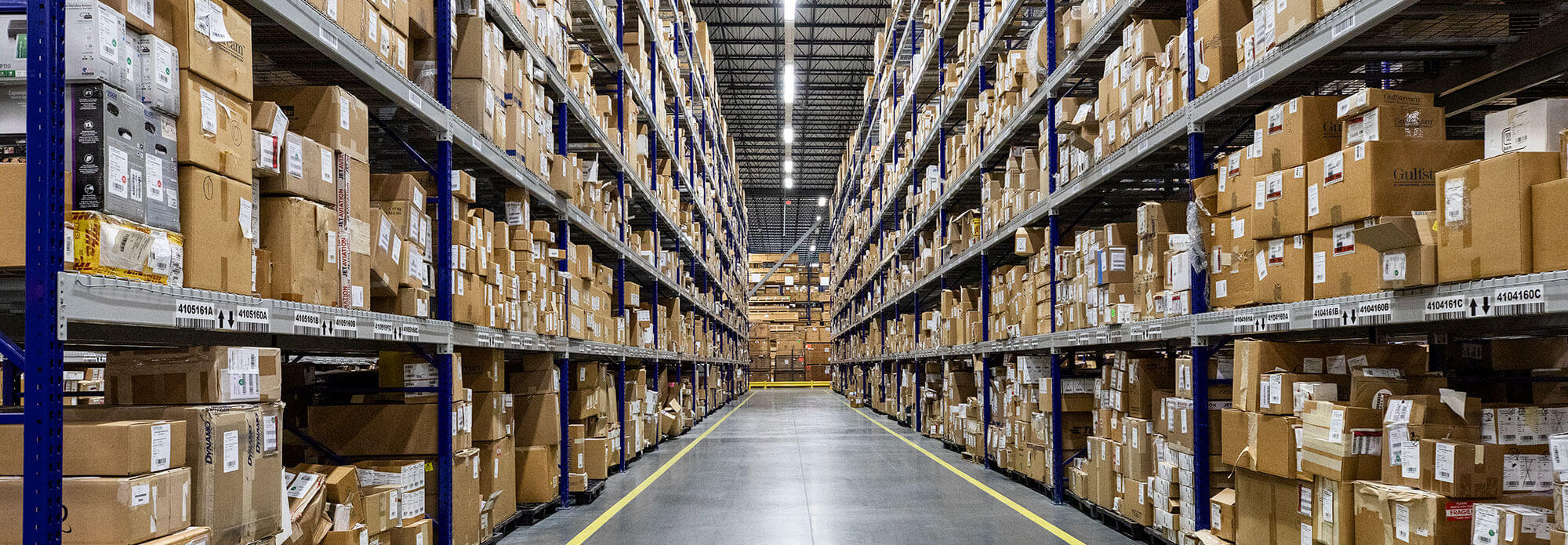 View down a Parts Distribution Warehouse aisle stacked floor to ceiling with labeled boxes.