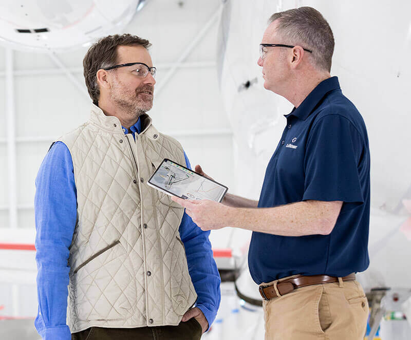 Gulfstream Customer Support employees in a service hangar discuss aircraft data on a tablet.